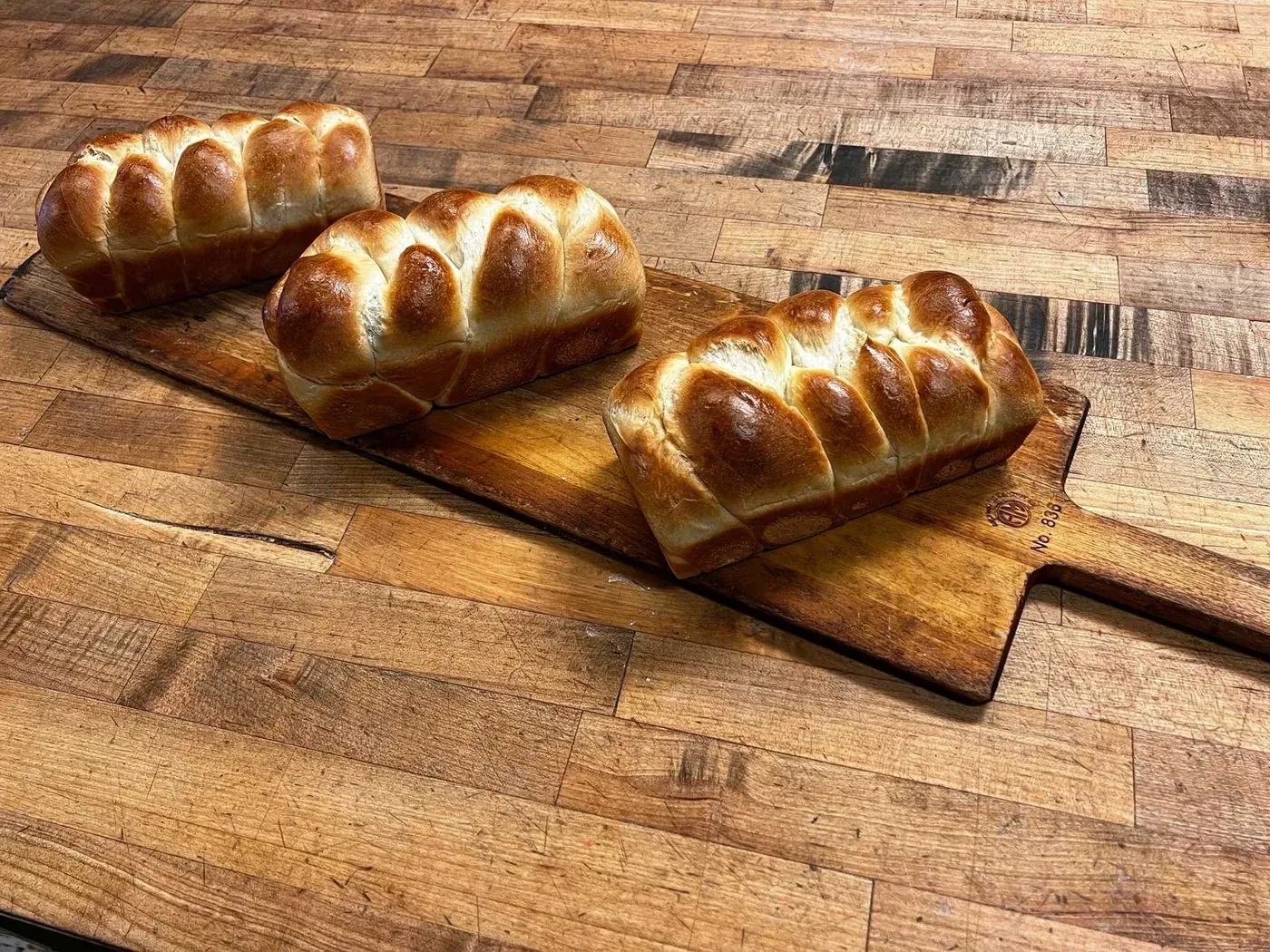 Three braided brioche loaves on a wooden serving board